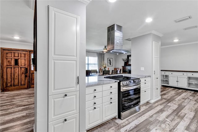 kitchen featuring light stone counters, ornamental molding, wall chimney exhaust hood, white cabinets, and stainless steel range with electric cooktop