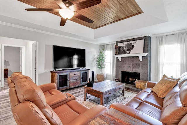 living room with a tray ceiling, a tiled fireplace, crown molding, and wooden ceiling