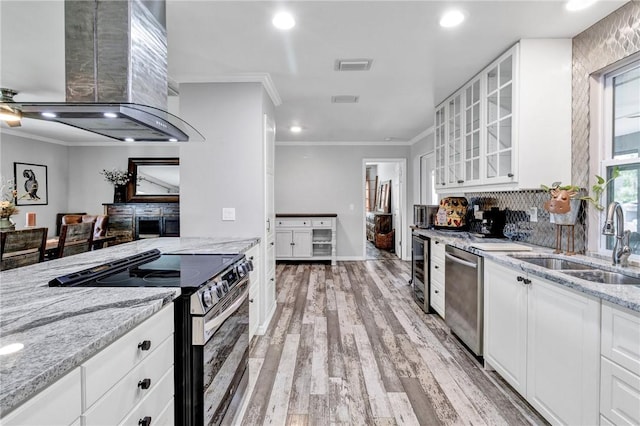 kitchen with sink, range hood, appliances with stainless steel finishes, light stone counters, and white cabinetry