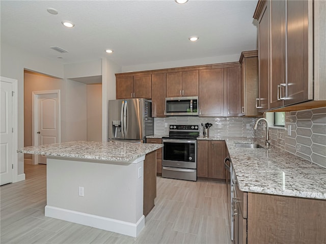 kitchen featuring stainless steel appliances, sink, a kitchen island, and light stone countertops