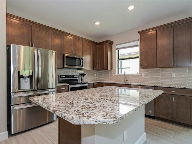 kitchen with light wood-type flooring, light stone countertops, a kitchen island, and appliances with stainless steel finishes