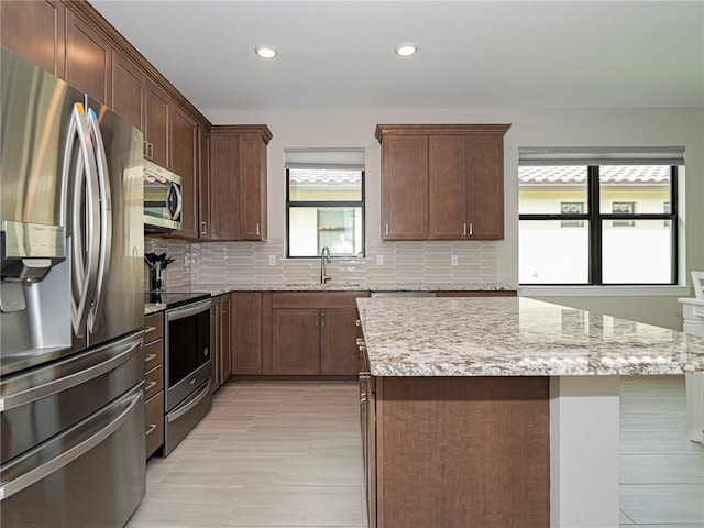 kitchen with a kitchen island, backsplash, appliances with stainless steel finishes, light stone countertops, and sink