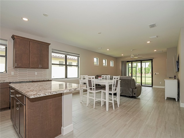 kitchen with light stone counters, tasteful backsplash, ceiling fan, dark brown cabinets, and a center island