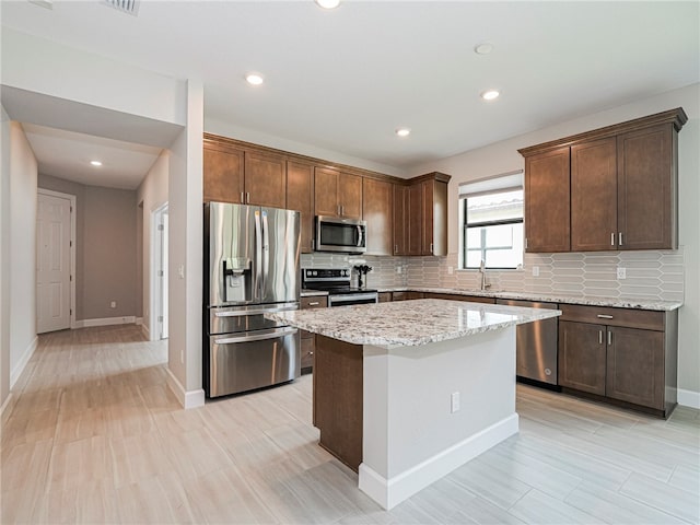 kitchen featuring appliances with stainless steel finishes, light stone counters, a kitchen island, and backsplash