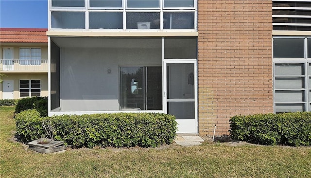 view of exterior entry featuring a yard and brick siding