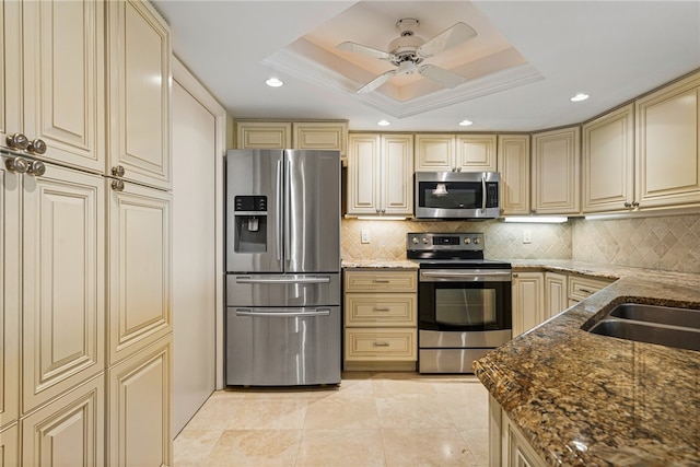 kitchen featuring cream cabinetry, stainless steel appliances, dark stone countertops, and a tray ceiling