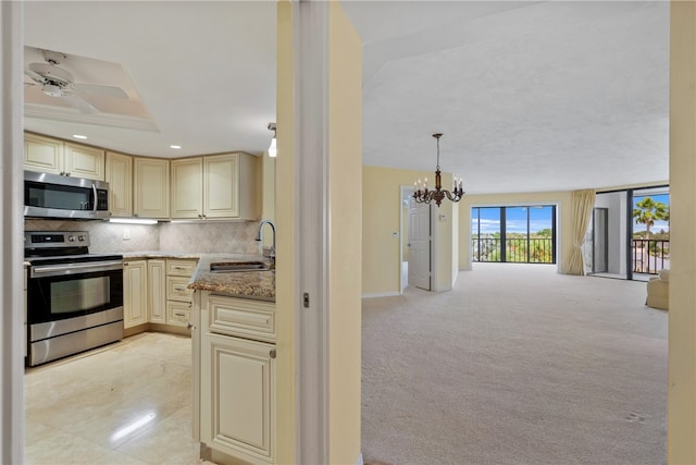 kitchen with appliances with stainless steel finishes, light stone countertops, hanging light fixtures, sink, and cream cabinetry