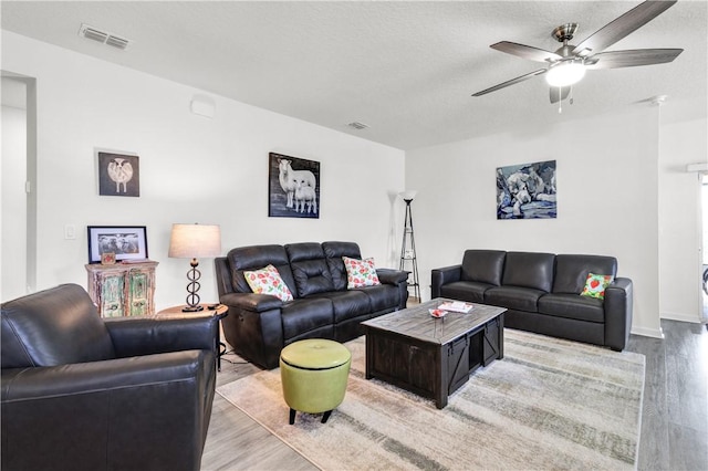 living room featuring ceiling fan, a textured ceiling, and light wood-type flooring