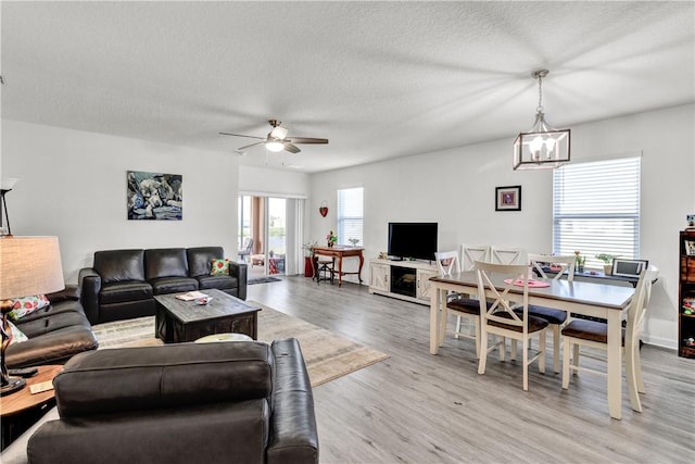 living room featuring ceiling fan with notable chandelier, light hardwood / wood-style floors, and a textured ceiling