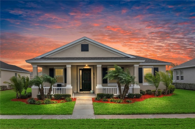 view of front of home with a shingled roof, a front lawn, covered porch, and stucco siding