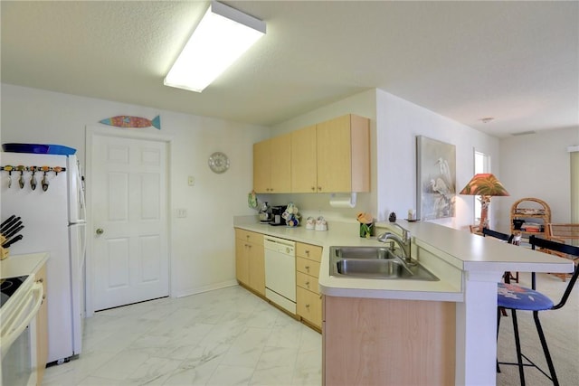 kitchen with a breakfast bar, white appliances, sink, light brown cabinetry, and kitchen peninsula