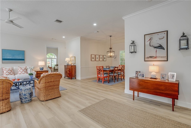 living area with wood finished floors, visible vents, baseboards, ornamental molding, and an inviting chandelier