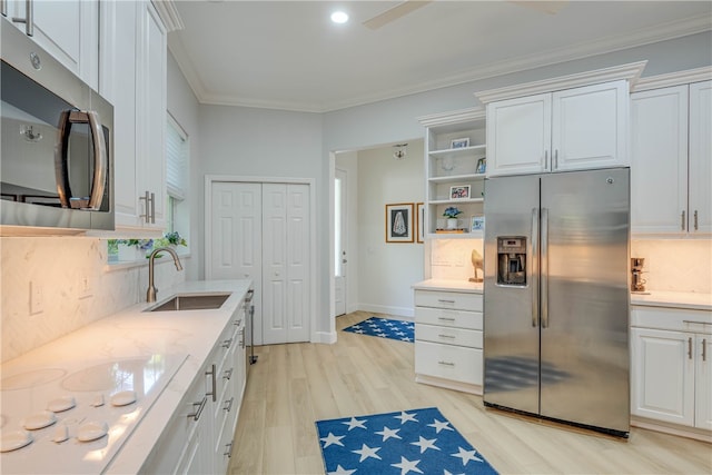 kitchen with light wood-style flooring, ornamental molding, stainless steel appliances, white cabinetry, and a sink