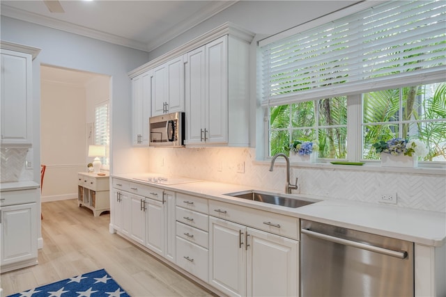 kitchen with light wood-style flooring, a sink, ornamental molding, appliances with stainless steel finishes, and tasteful backsplash