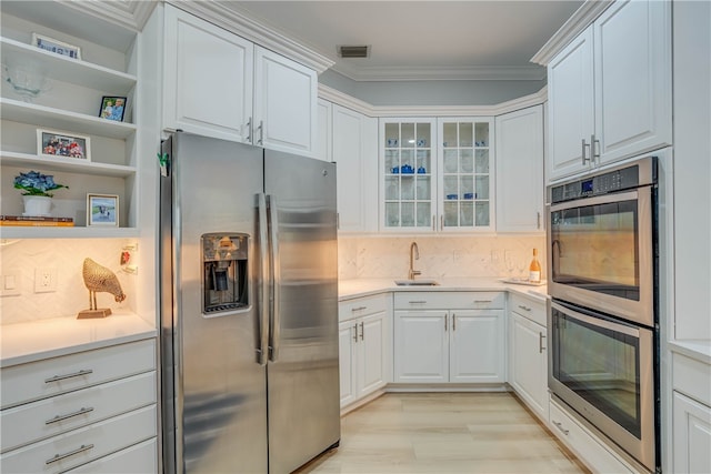 kitchen featuring appliances with stainless steel finishes, light countertops, white cabinets, and ornamental molding