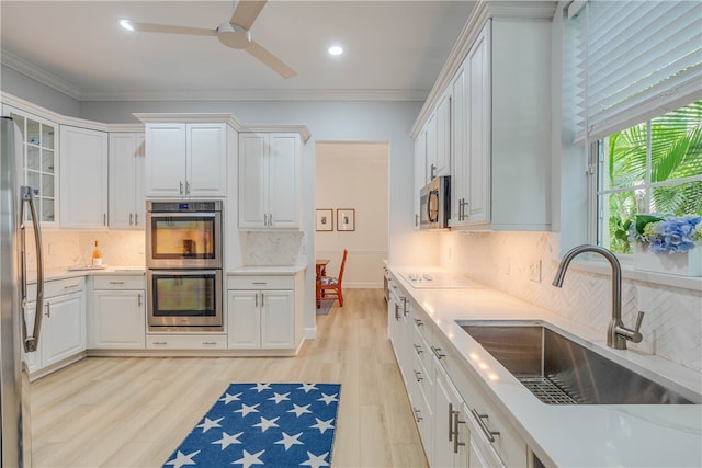 kitchen with stainless steel appliances, light countertops, crown molding, and a sink