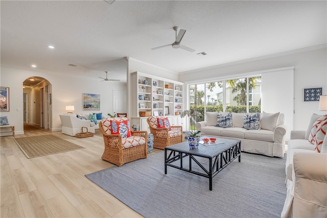 living room with visible vents, arched walkways, a ceiling fan, light wood-style flooring, and crown molding