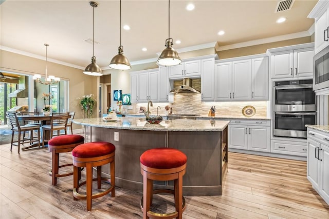 kitchen featuring pendant lighting, light hardwood / wood-style floors, a kitchen island with sink, and double oven