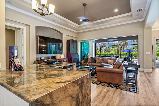 living room featuring ceiling fan with notable chandelier, a tray ceiling, light hardwood / wood-style flooring, and ornamental molding