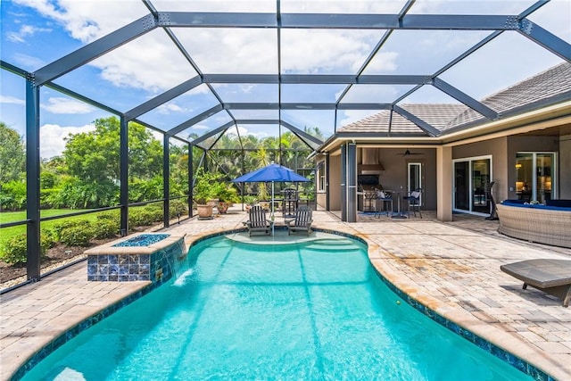 view of swimming pool with glass enclosure, an outdoor kitchen, pool water feature, ceiling fan, and a patio area