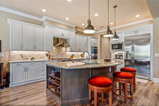 kitchen featuring light wood-type flooring, a kitchen island with sink, built in appliances, white cabinetry, and range hood