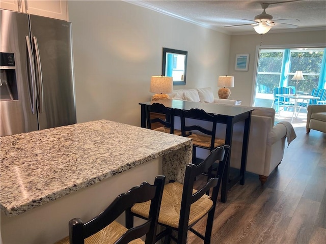 kitchen with stainless steel fridge, light stone countertops, crown molding, and white cabinetry