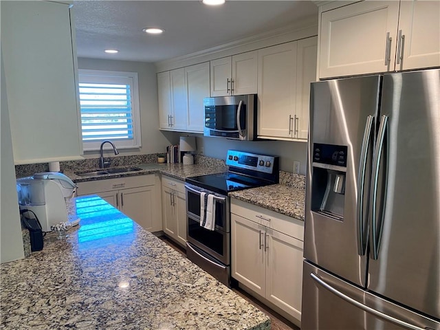 kitchen featuring white cabinets, stainless steel appliances, light stone countertops, and sink