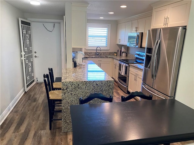 kitchen featuring white cabinets, appliances with stainless steel finishes, a kitchen bar, and sink