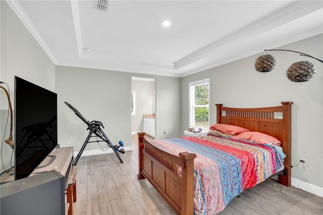 bedroom with a raised ceiling, crown molding, connected bathroom, and light wood-type flooring