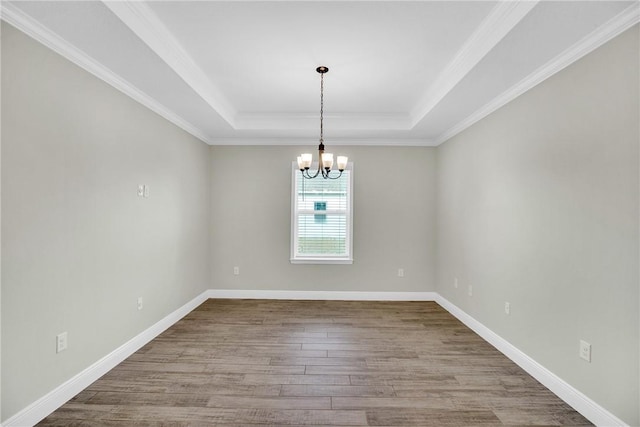 unfurnished room with an inviting chandelier, hardwood / wood-style flooring, ornamental molding, and a raised ceiling