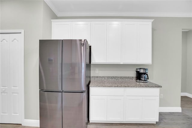 kitchen with crown molding, light stone counters, stainless steel refrigerator, light hardwood / wood-style floors, and white cabinets