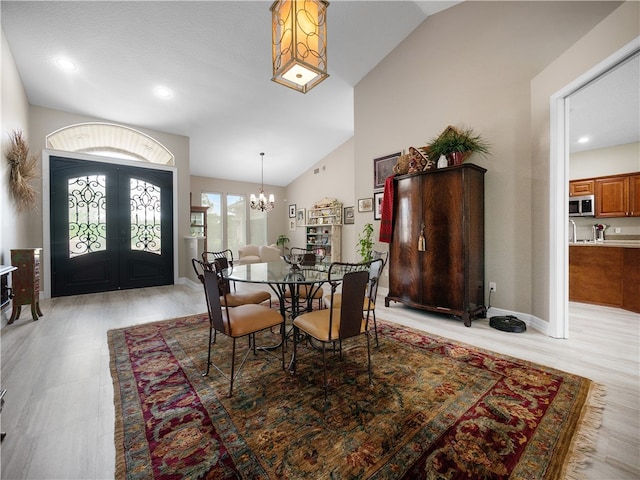 dining space with a chandelier, light wood-type flooring, lofted ceiling, and french doors