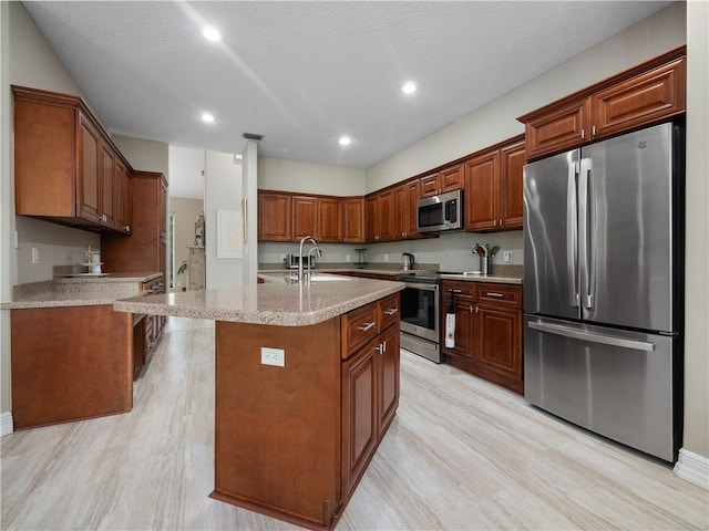 kitchen featuring stainless steel appliances, light wood-type flooring, a textured ceiling, sink, and an island with sink