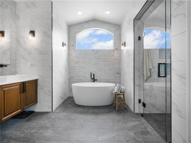 bathroom featuring tile walls, vanity, shower with separate bathtub, and vaulted ceiling