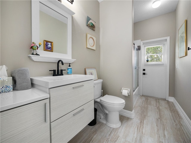 full bathroom with toilet, hardwood / wood-style floors, a textured ceiling, combined bath / shower with glass door, and vanity