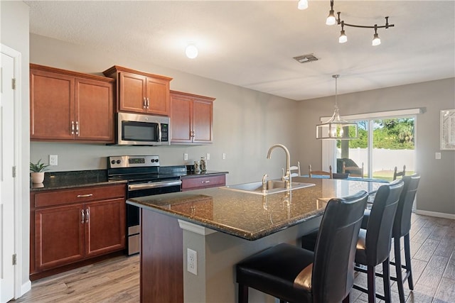 kitchen with light wood-type flooring, stainless steel appliances, sink, a center island with sink, and a breakfast bar area