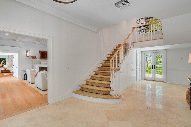 foyer featuring french doors, a notable chandelier, ornamental molding, beamed ceiling, and light wood-type flooring