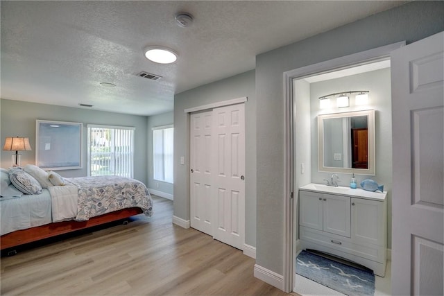 bedroom with a textured ceiling, light hardwood / wood-style floors, ensuite bathroom, and sink