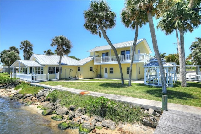 back of property with a gazebo, a balcony, a water view, and a lawn