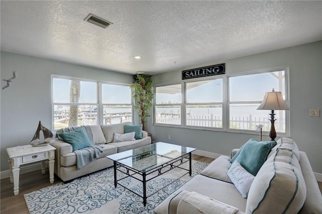 living room with a textured ceiling, a water view, a wealth of natural light, and light hardwood / wood-style floors