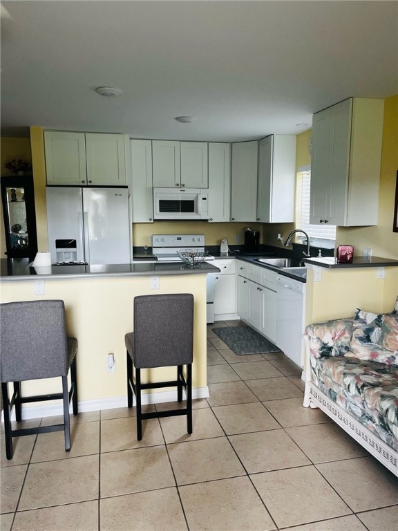 kitchen featuring white cabinetry, sink, a kitchen bar, light tile patterned floors, and white appliances