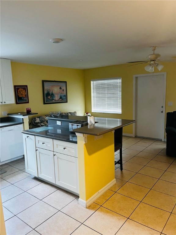 kitchen with a kitchen bar, light tile patterned floors, ceiling fan, a kitchen island, and white cabinetry