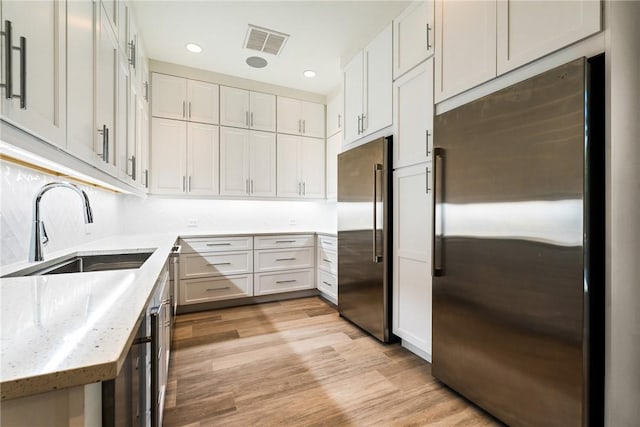 kitchen with visible vents, light stone countertops, stainless steel fridge, high end fridge, and a sink