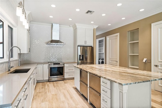 kitchen featuring visible vents, a kitchen island, stainless steel appliances, wall chimney exhaust hood, and a sink