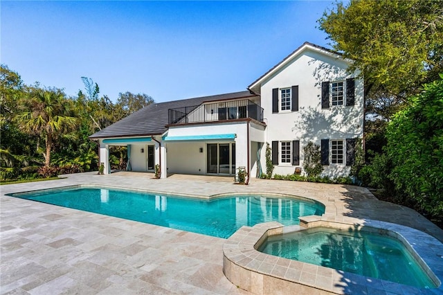 rear view of property with stucco siding, a patio, a balcony, and a pool with connected hot tub