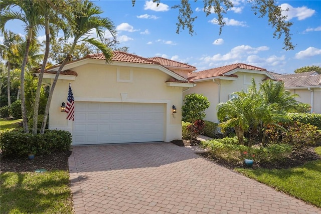 mediterranean / spanish home with decorative driveway, a tiled roof, an attached garage, and stucco siding