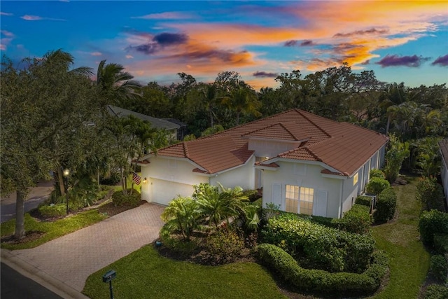 view of front of home featuring decorative driveway, a tile roof, stucco siding, an attached garage, and a front yard