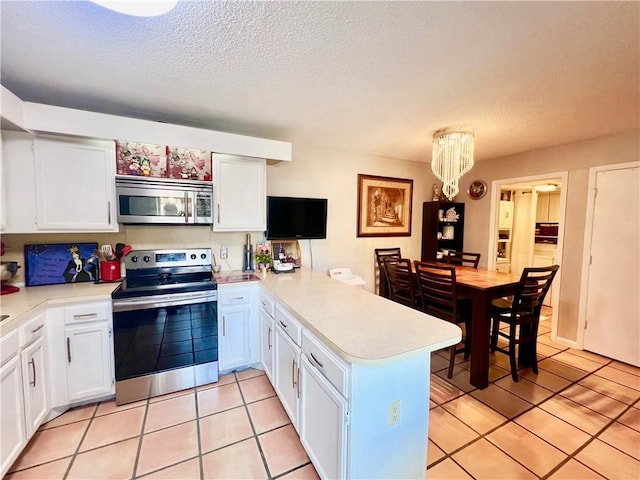 kitchen with appliances with stainless steel finishes, white cabinetry, light tile patterned floors, kitchen peninsula, and a textured ceiling