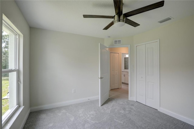 unfurnished bedroom featuring ceiling fan, a closet, light carpet, and multiple windows