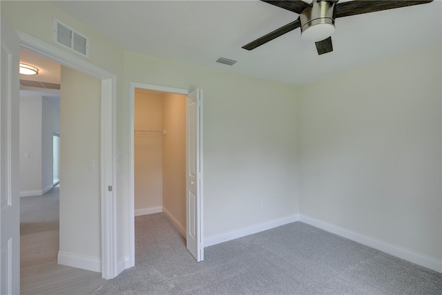 unfurnished bedroom with ceiling fan, a spacious closet, light carpet, and a closet